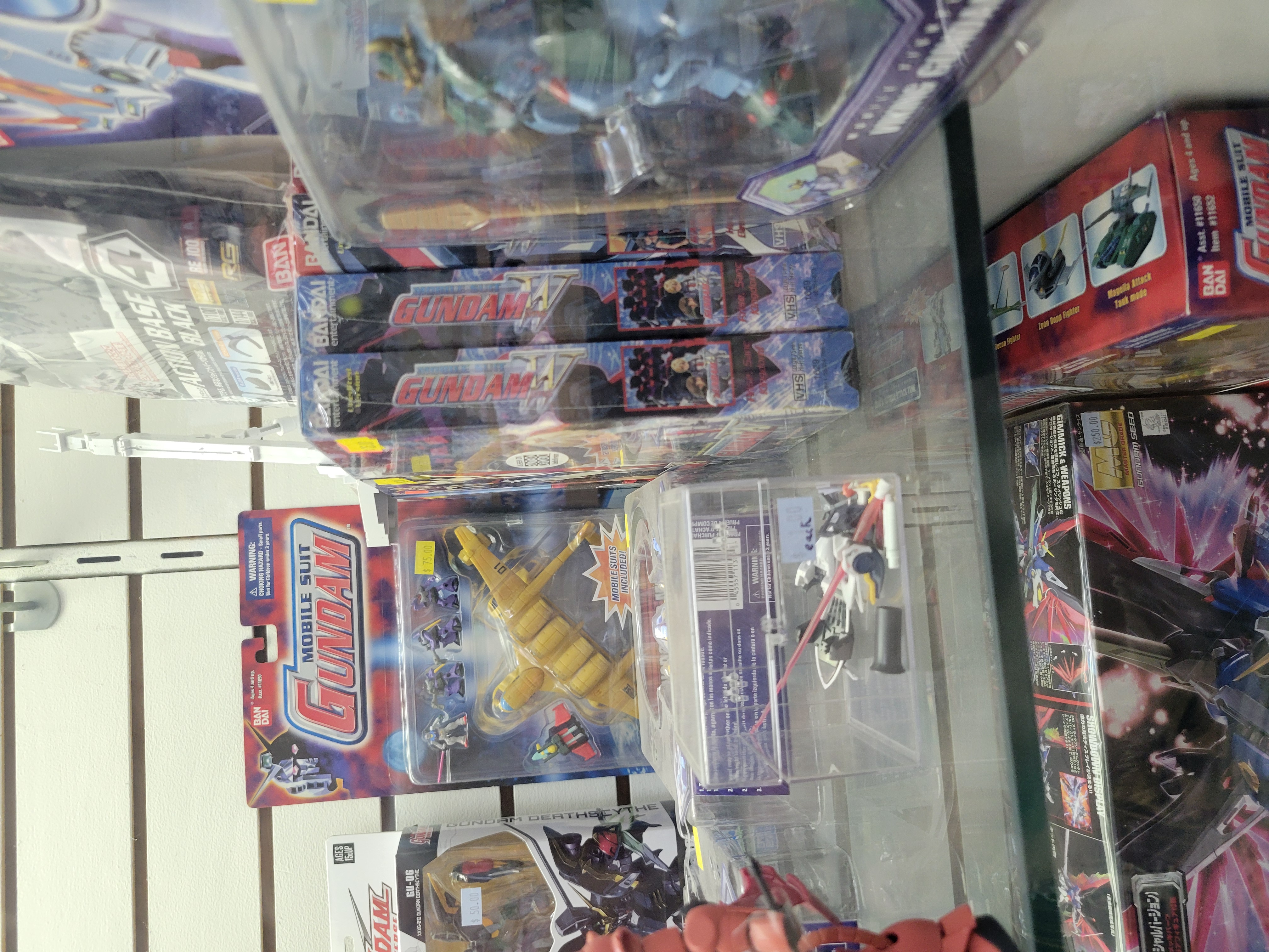 Glass case filled with gundam toys and gundam wing tape videos.
